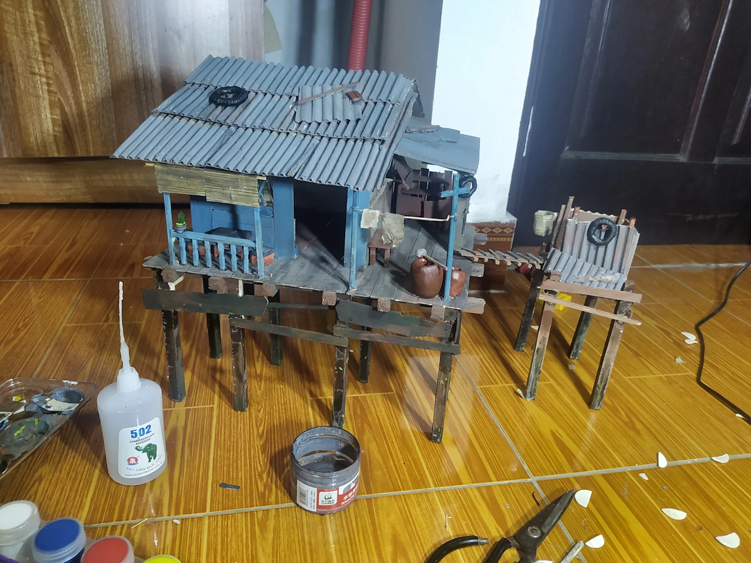 Miniature wooden house model on stilts for fish tank decoration with crafting supplies nearby
